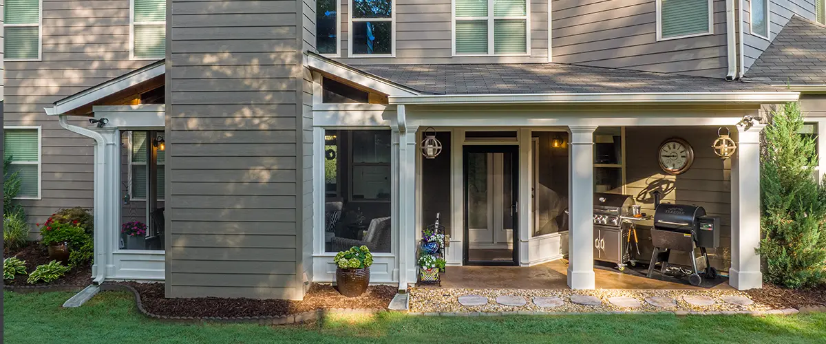 Backyard covered porch and screened room addition with white columns and landscaped lawn.