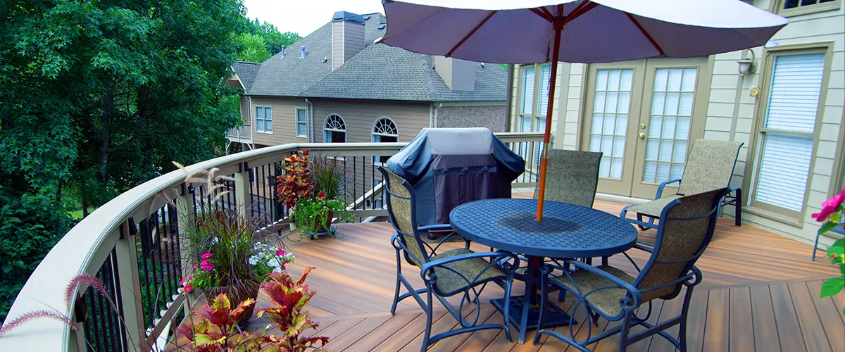 Composite backyard deck with curved railing, outdoor dining set, umbrella and built-in space for grilling.