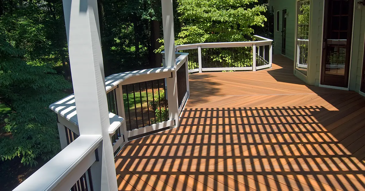 Composite deck with white and black railings, pergola shade and wooded backyard views.
