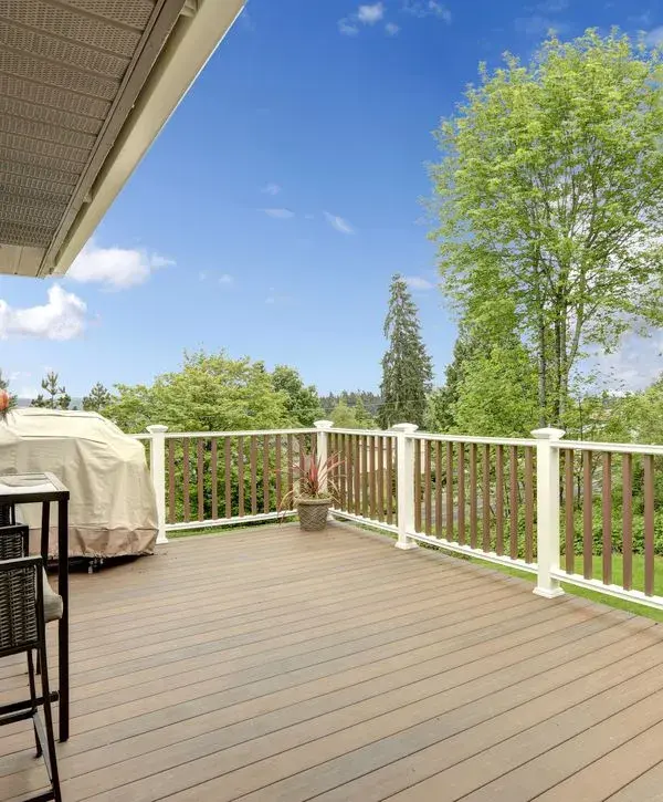 Composite deck with white railings, outdoor grill and scenic backyard views.