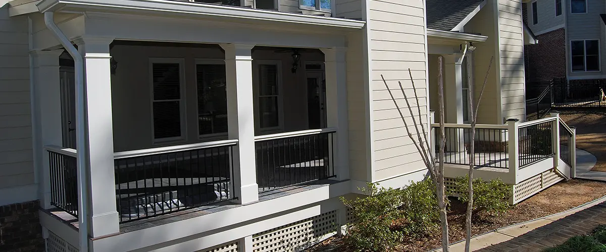 Covered back porch with white columns, black railings and dual chimney features on a two-story home.