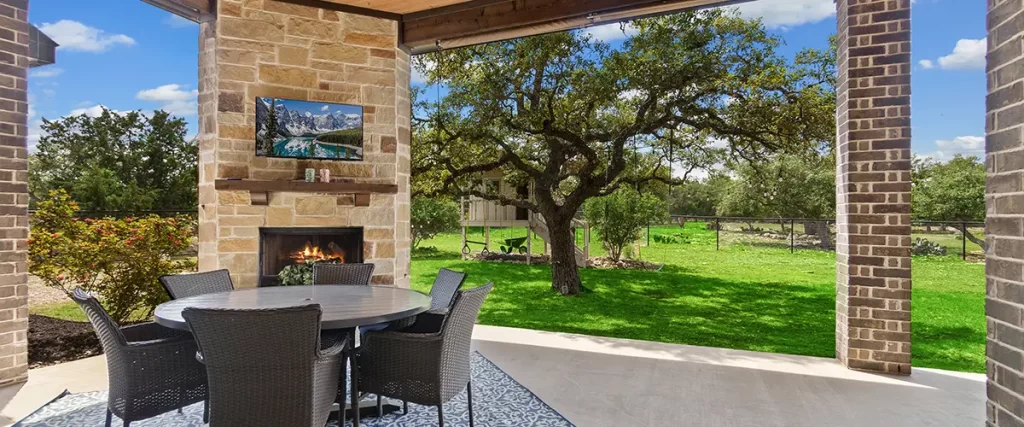 Covered patio with outdoor fireplace, dining area, wood ceiling and spacious backyard views.