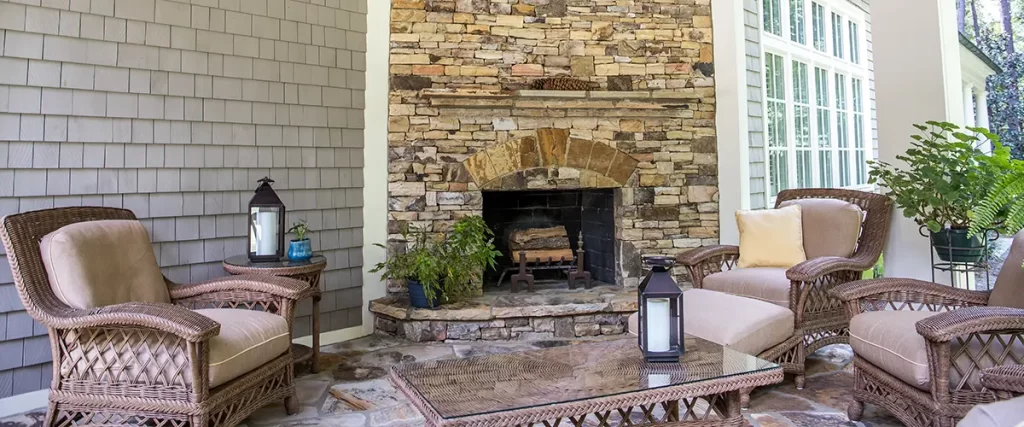 Covered porch with stone fireplace, wicker seating, wood ceiling and comfortable outdoor living area.
