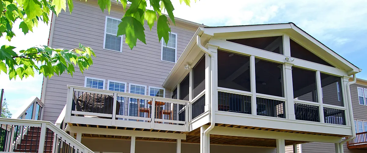 Elevated screened porch and deck addition with stairs, white trim and black railings.