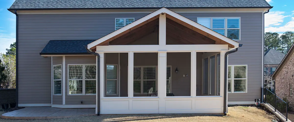 Gable-roof screened porch addition with white columns and spacious backyard outdoor living area.