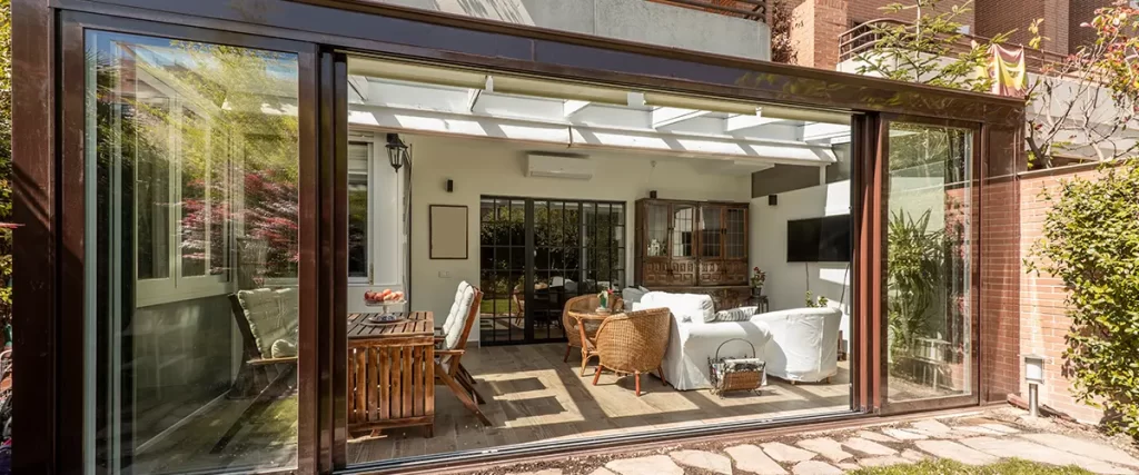 Modern glass sunroom addition with sliding doors, outdoor seating and direct access to the backyard.