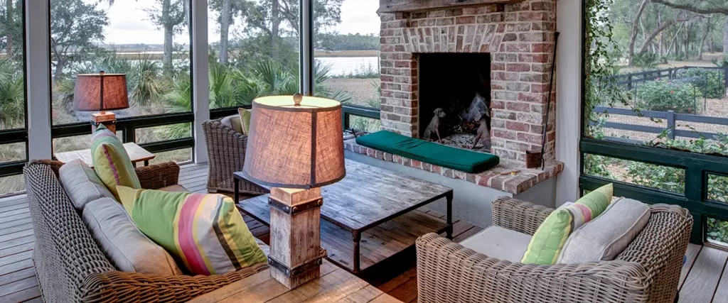 Screened-in porch with brick fireplace, vaulted ceiling, wicker furniture and scenic backyard views.