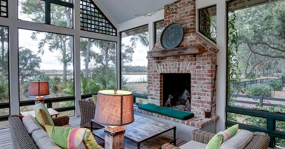 Screened-in porch with brick fireplace, vaulted ceiling, wicker furniture and scenic backyard views.