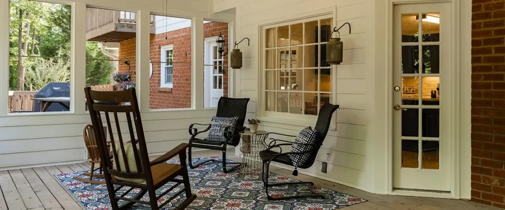 Screened-in porch with wood flooring, rocking chairs, ceiling fan and comfortable outdoor seating.