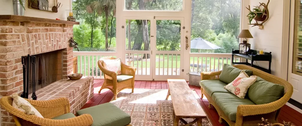 Screened porch with brick fireplace, wicker furniture, ceiling fan and views of a wooded backyard.