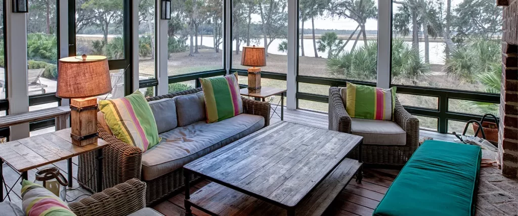 Screened porch with vaulted ceiling, wicker furniture and large windows overlooking a scenic waterfront.