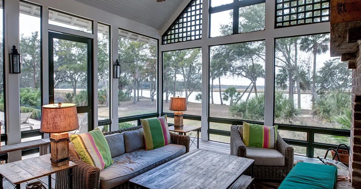 Screened porch with vaulted ceiling, wicker furniture and large windows overlooking a scenic waterfront.