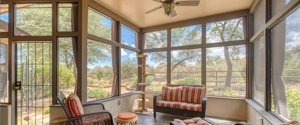 Screened porch with wicker seating, ceiling fan, tile flooring and large windows overlooking the backyard.