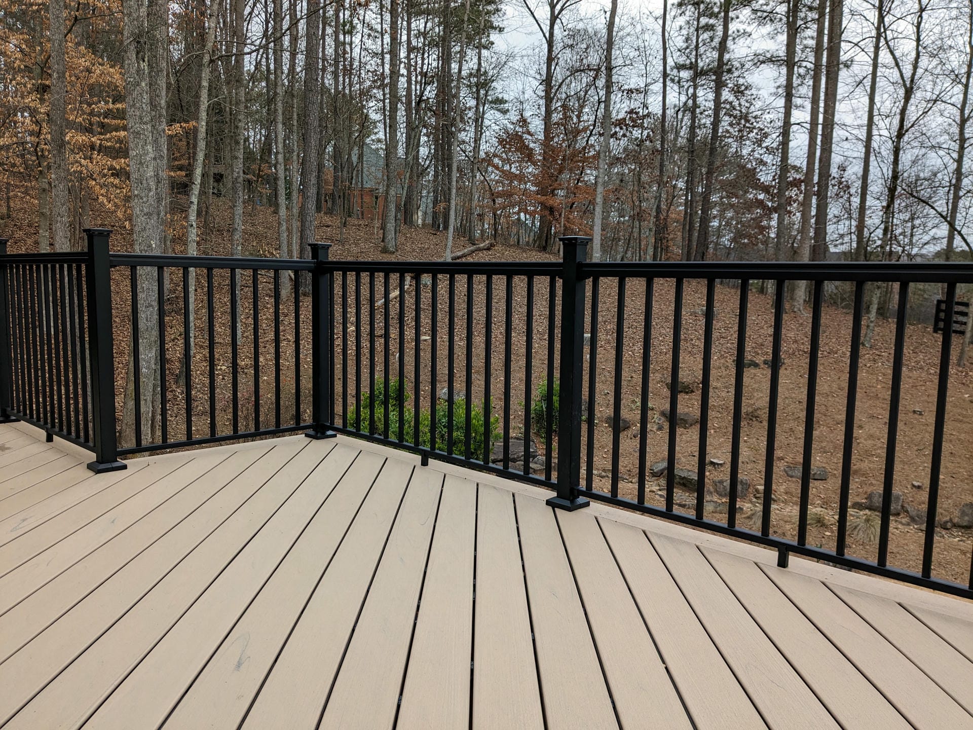 Black aluminum deck railing on a tan composite deck facing the woods