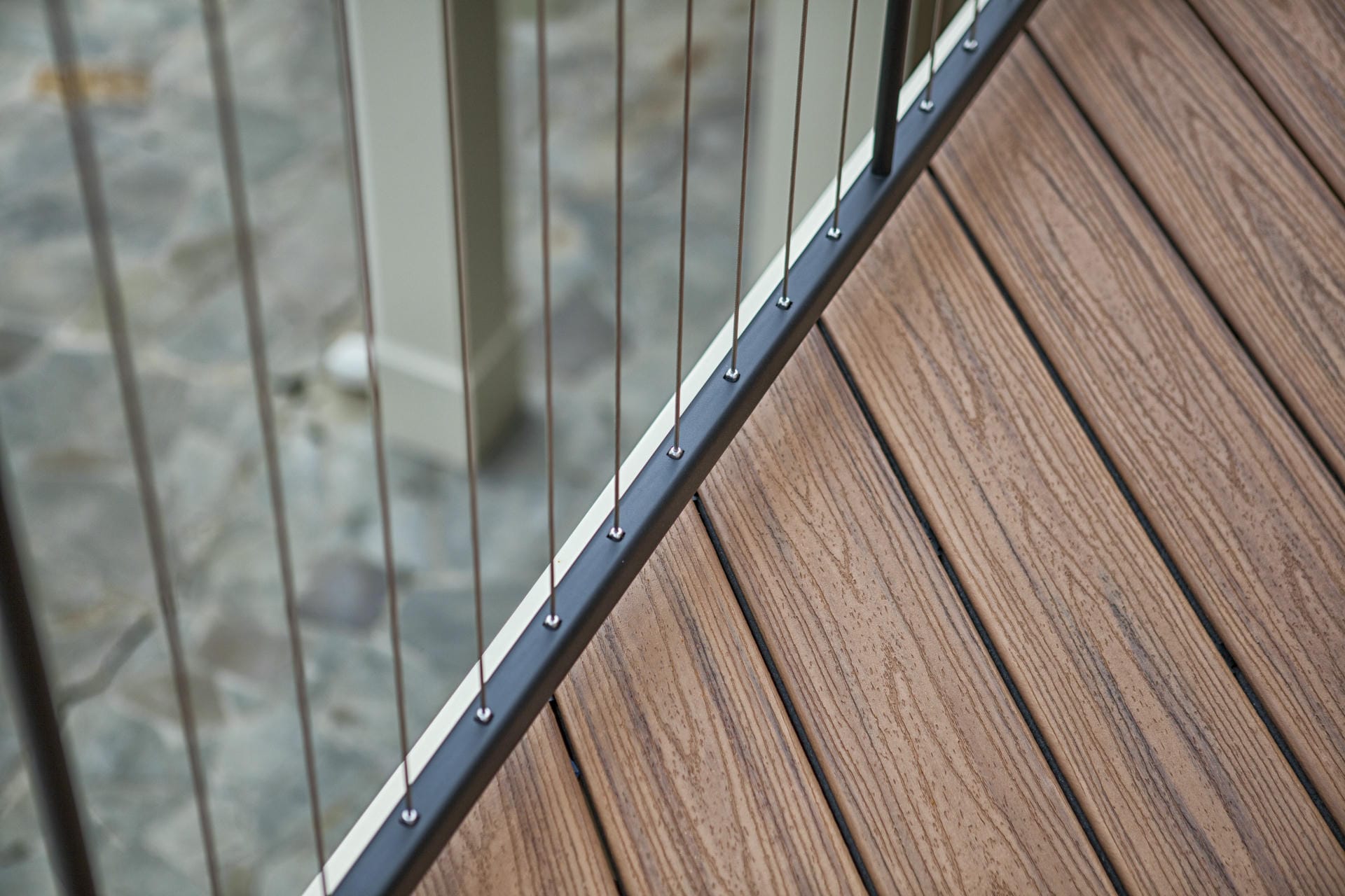 Close view of stainless steel cable terminations along a deck railing top rail