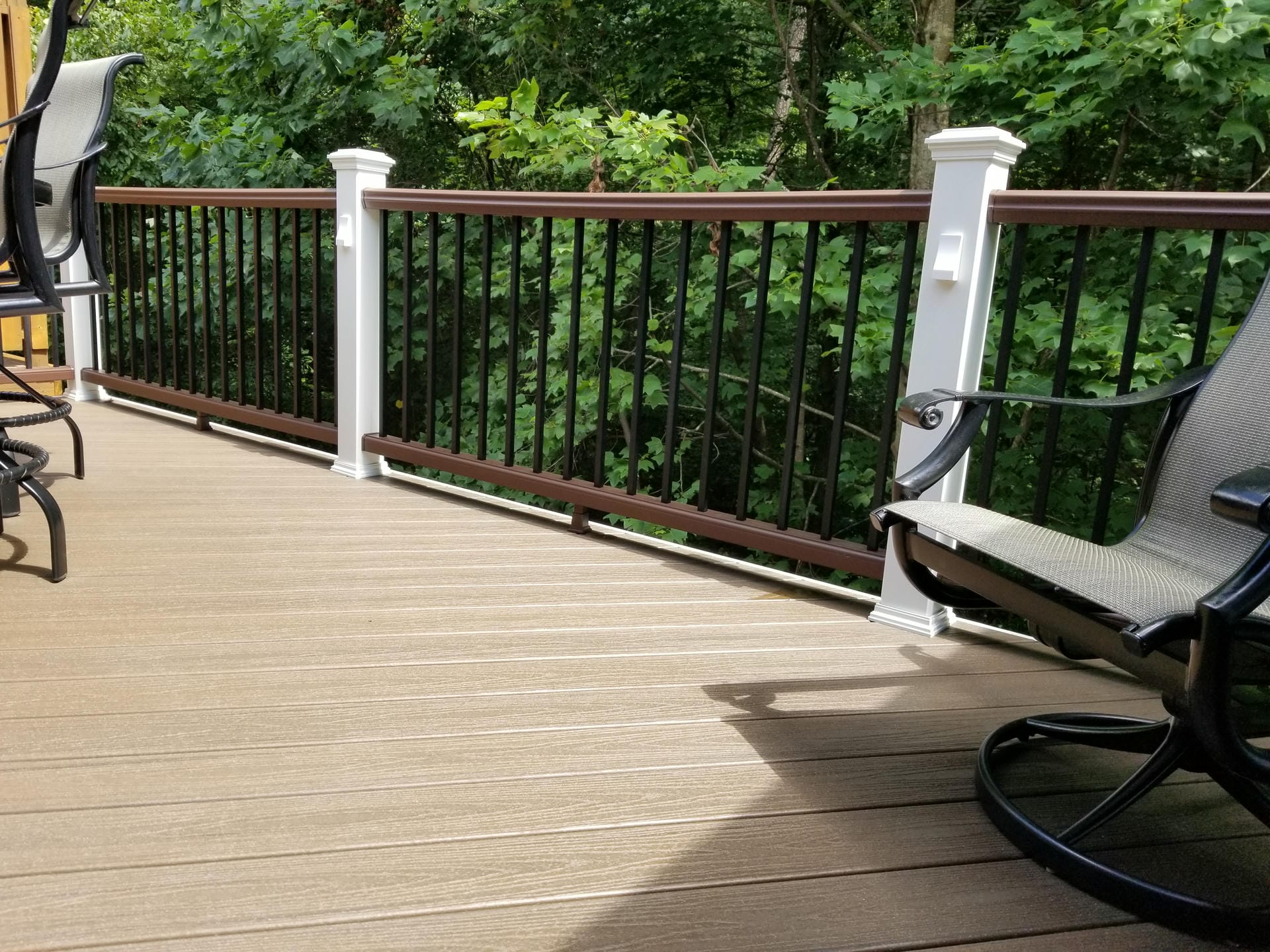 Composite deck railing with black balusters and a brown top rail beside patio chairs