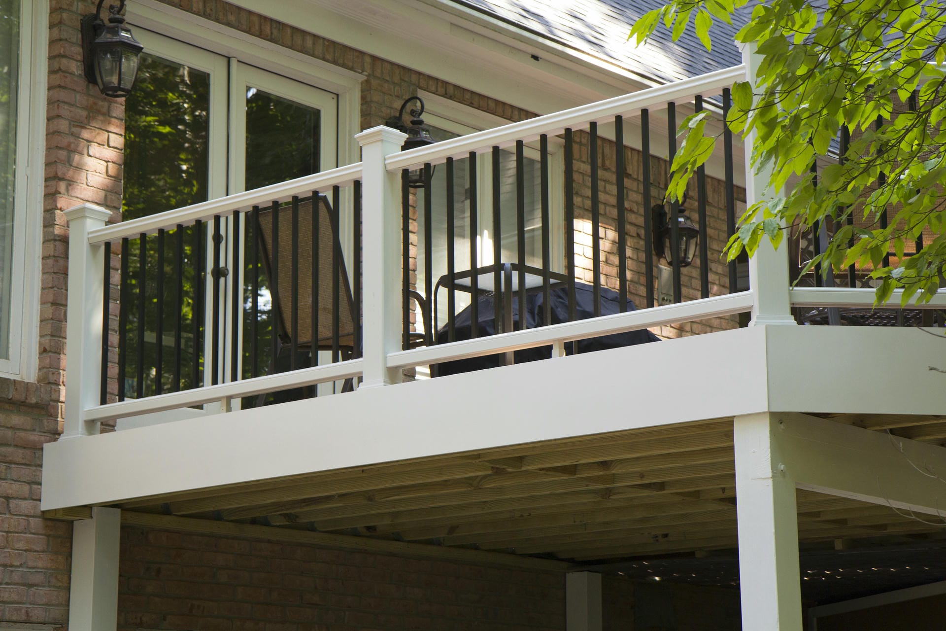 White deck railing with black balusters on an elevated deck above a finished ceiling