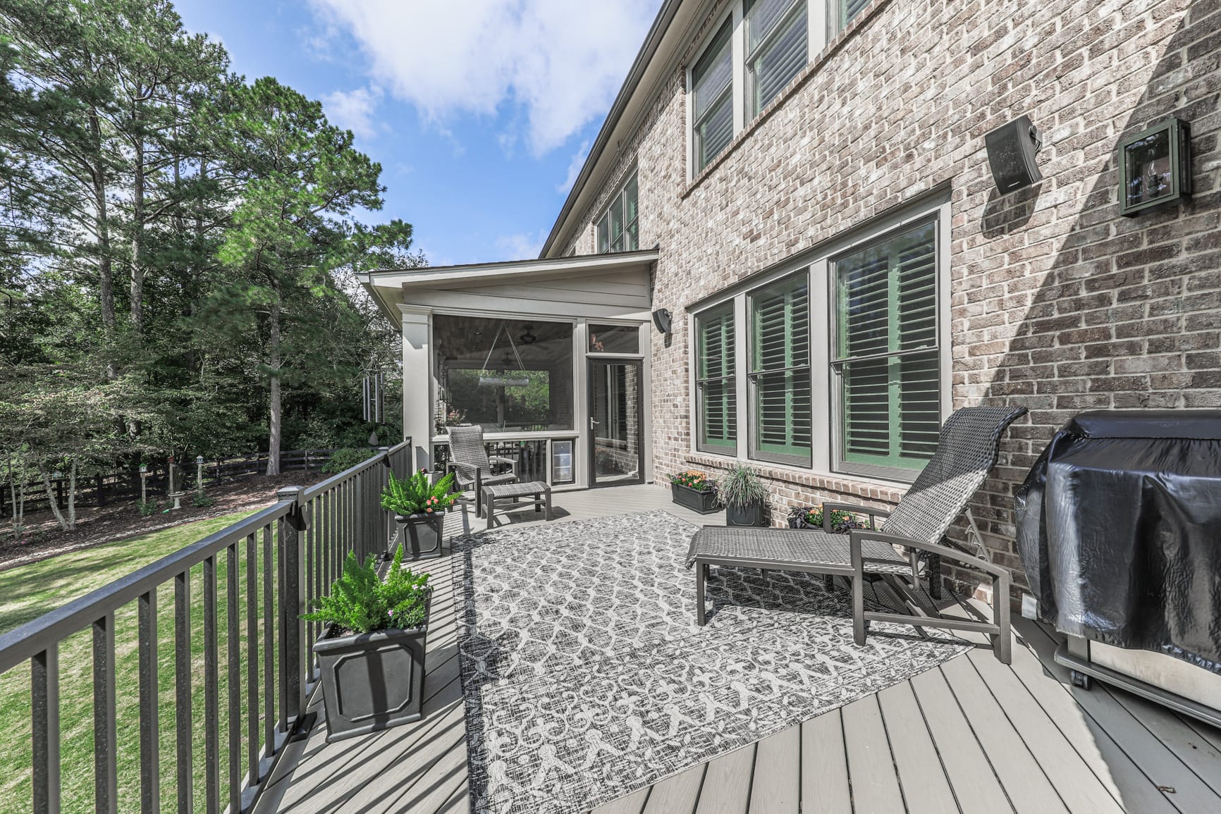 Grey composite deck and black railing beside a brick home and screened porch