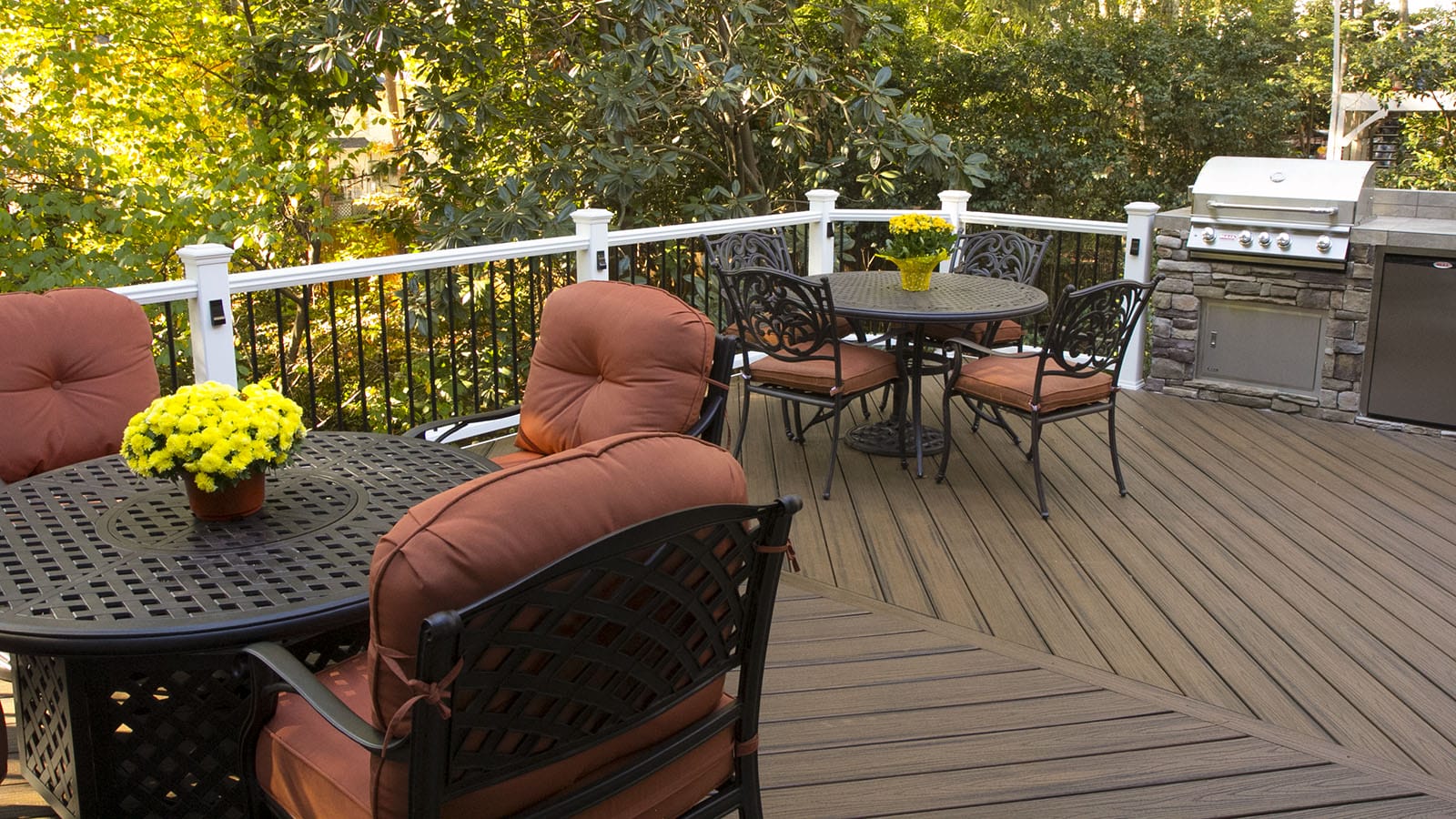 Composite deck furnished for autumn with white railing posts and a built in grill
