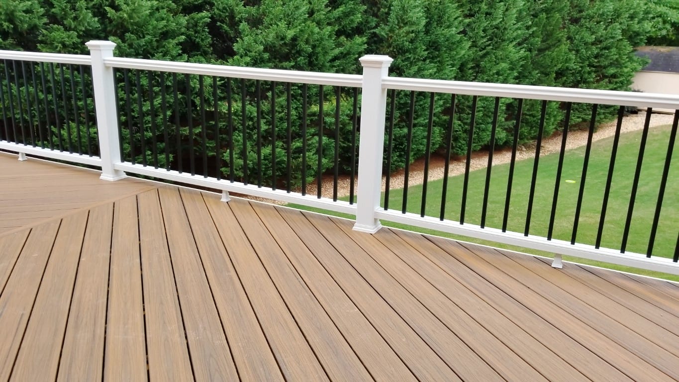 Deck railing with white posts and black balusters beside a manicured hedge