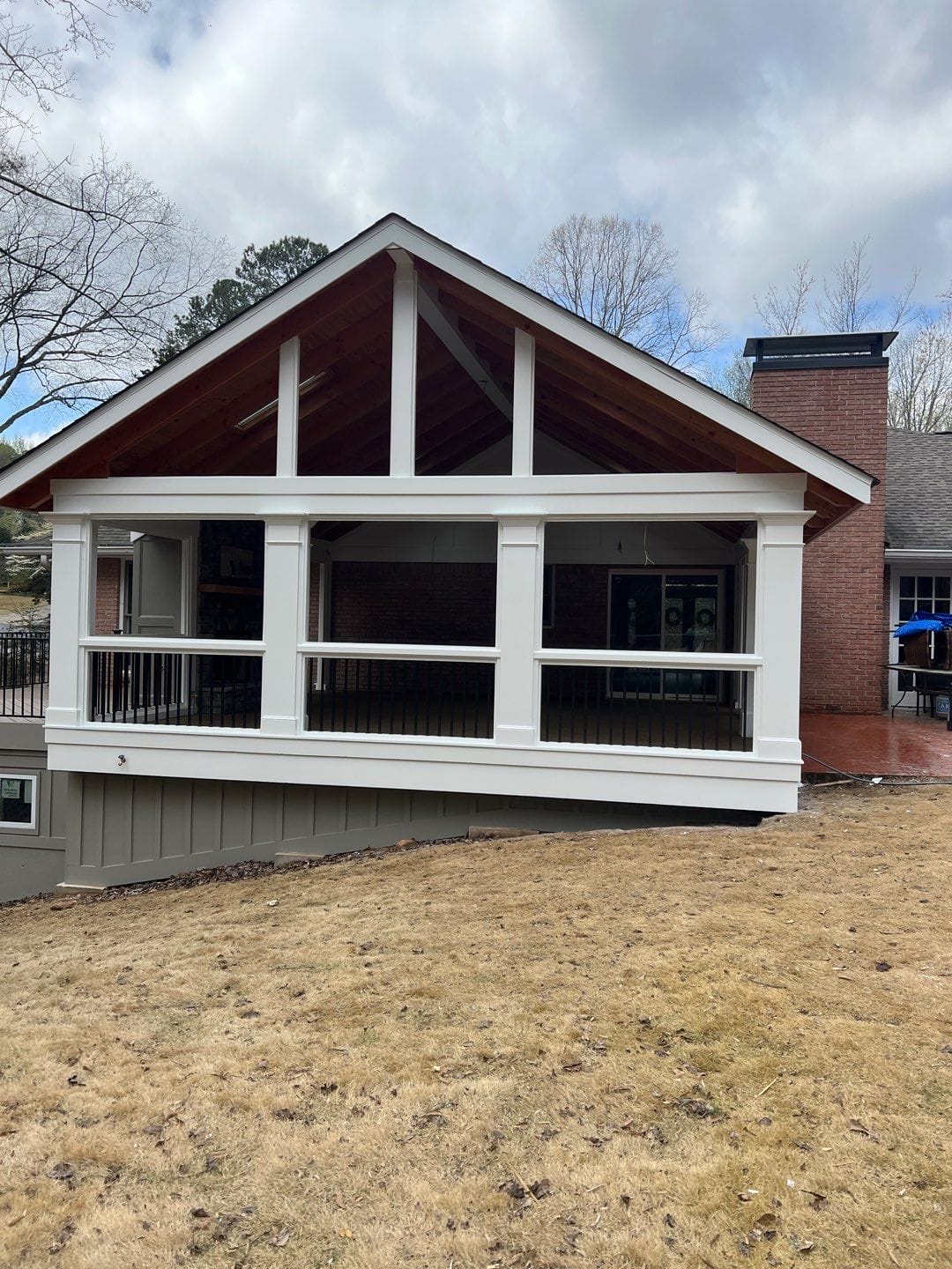 Screened porch with a gable roof and an exposed stained timber truss in the gable end