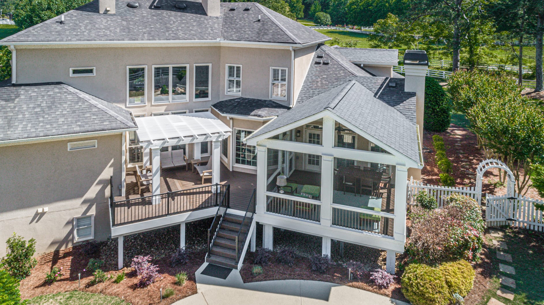 Aerial view of a gable roof screened porch beside a white pergola and deck