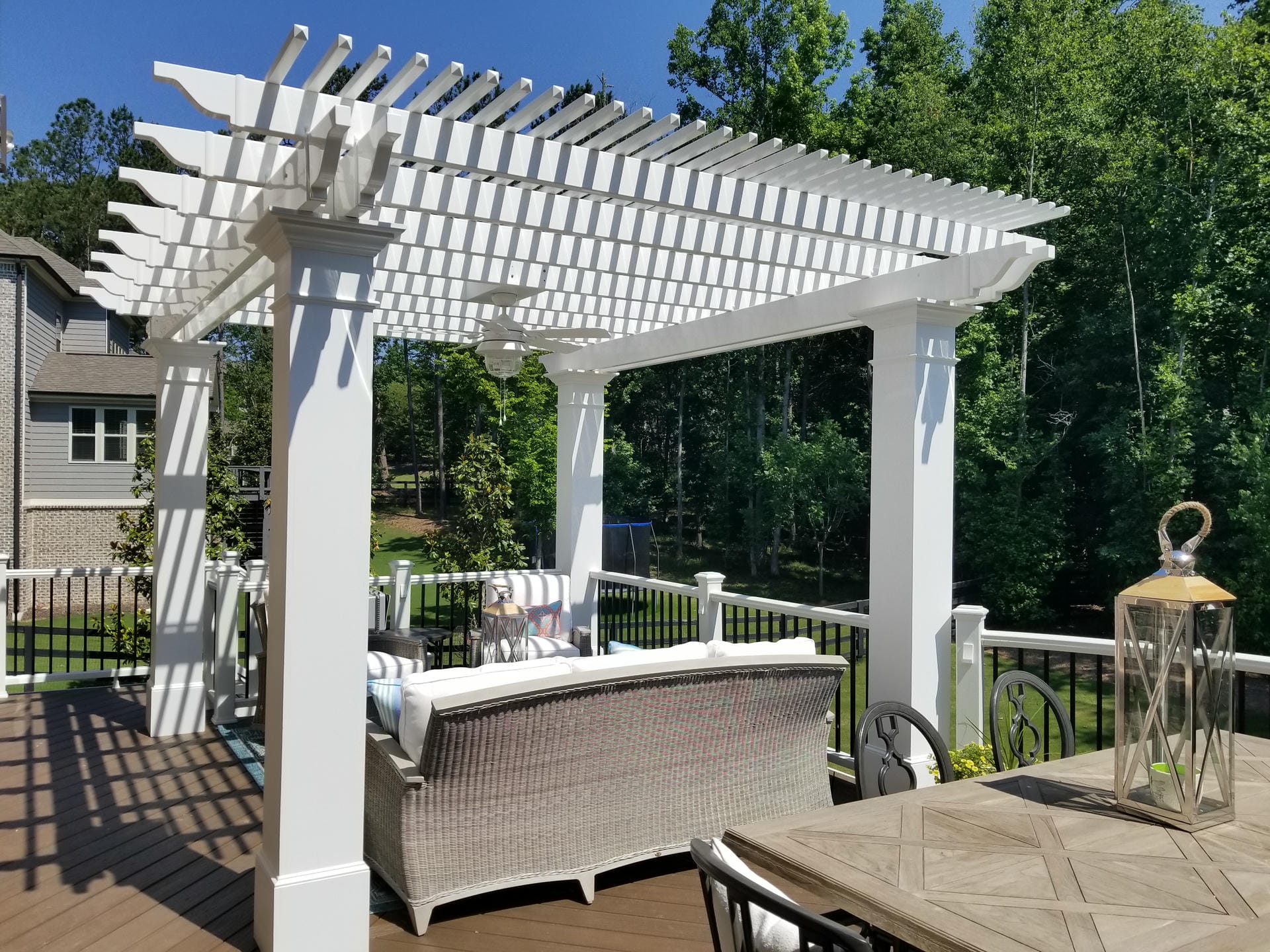 White pergola over a deck with wicker seating and a wooded view