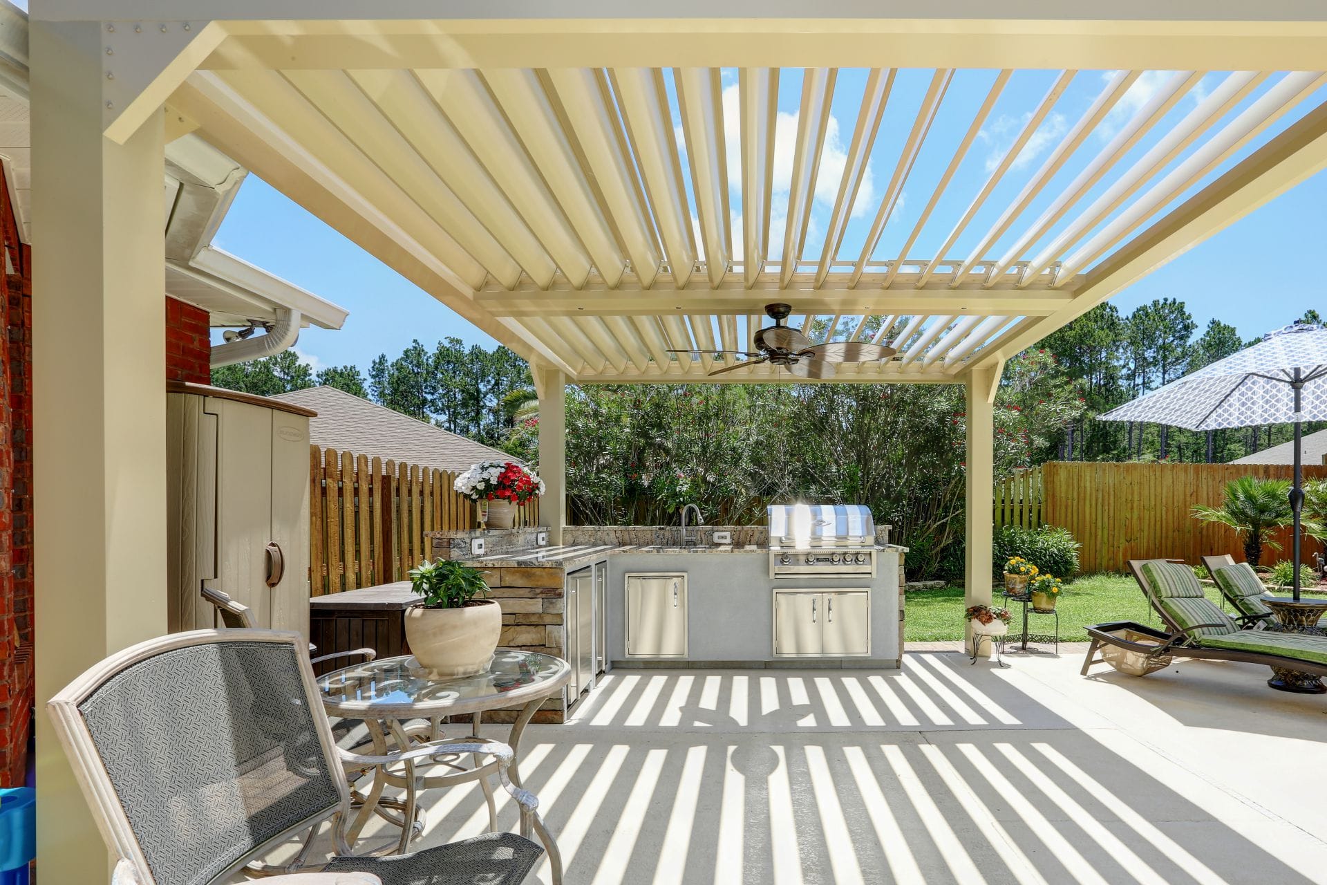 Adjustable louvers casting striped shade over an outdoor kitchen and grilling station