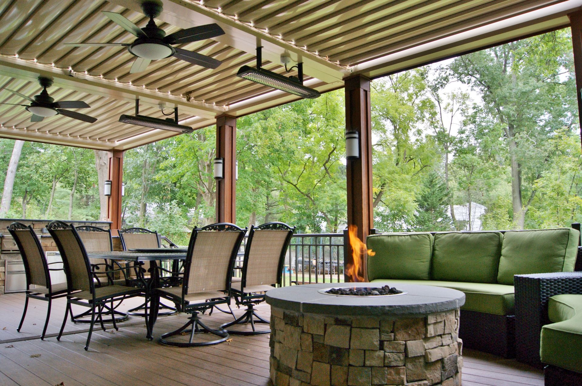 Louvered roof fitted with ceiling fans and mounted heaters above a deck fire pit