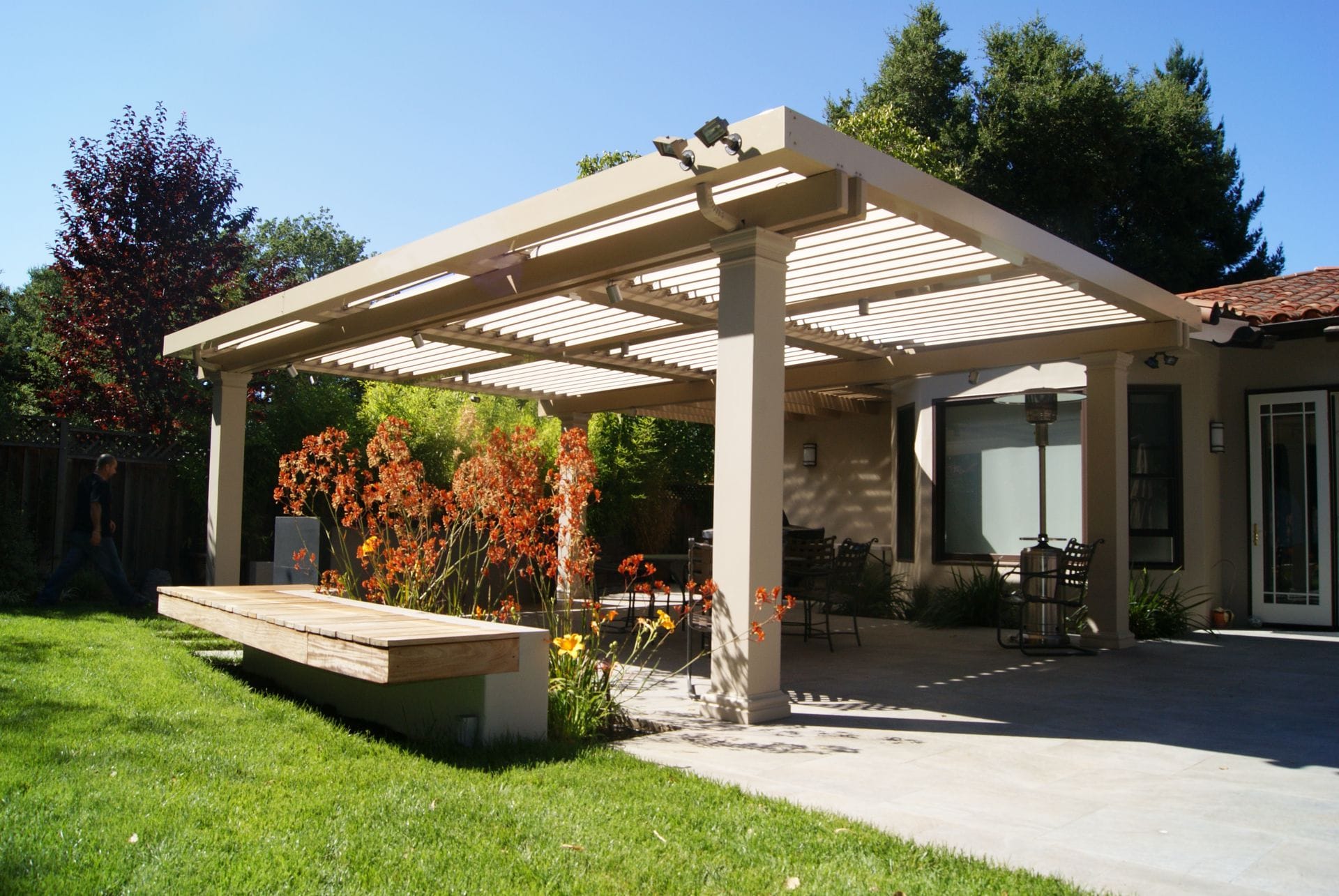 Freestanding louvered patio cover over a paved patio and garden
