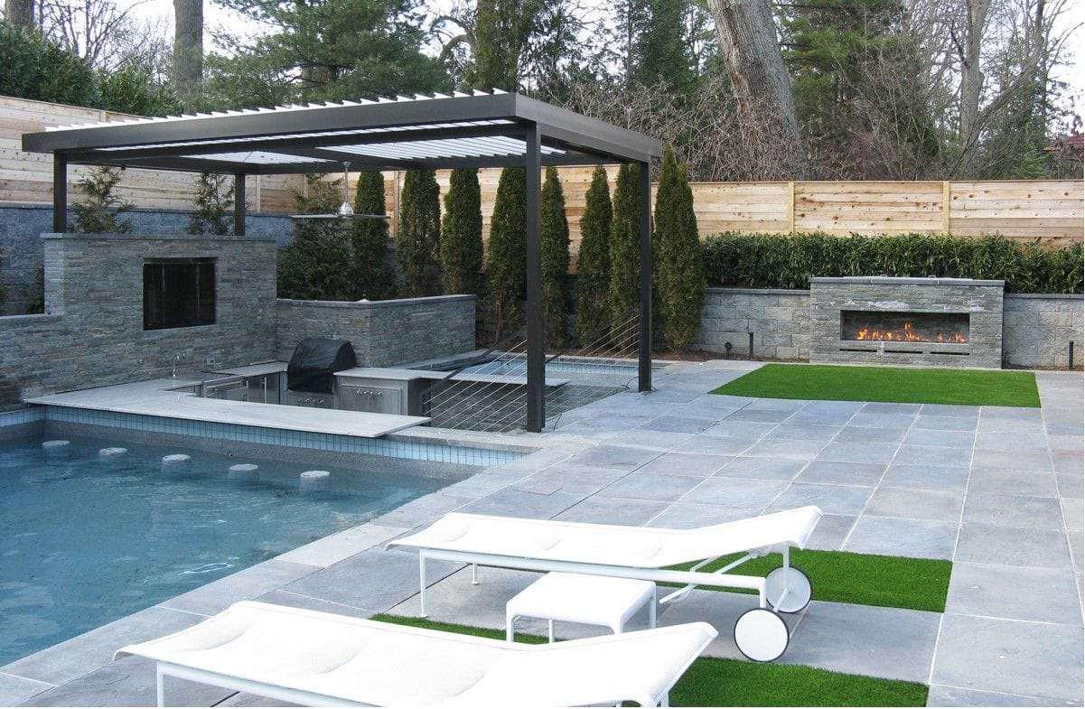 Freestanding black motorized pergola beside a pool with a linear gas fireplace