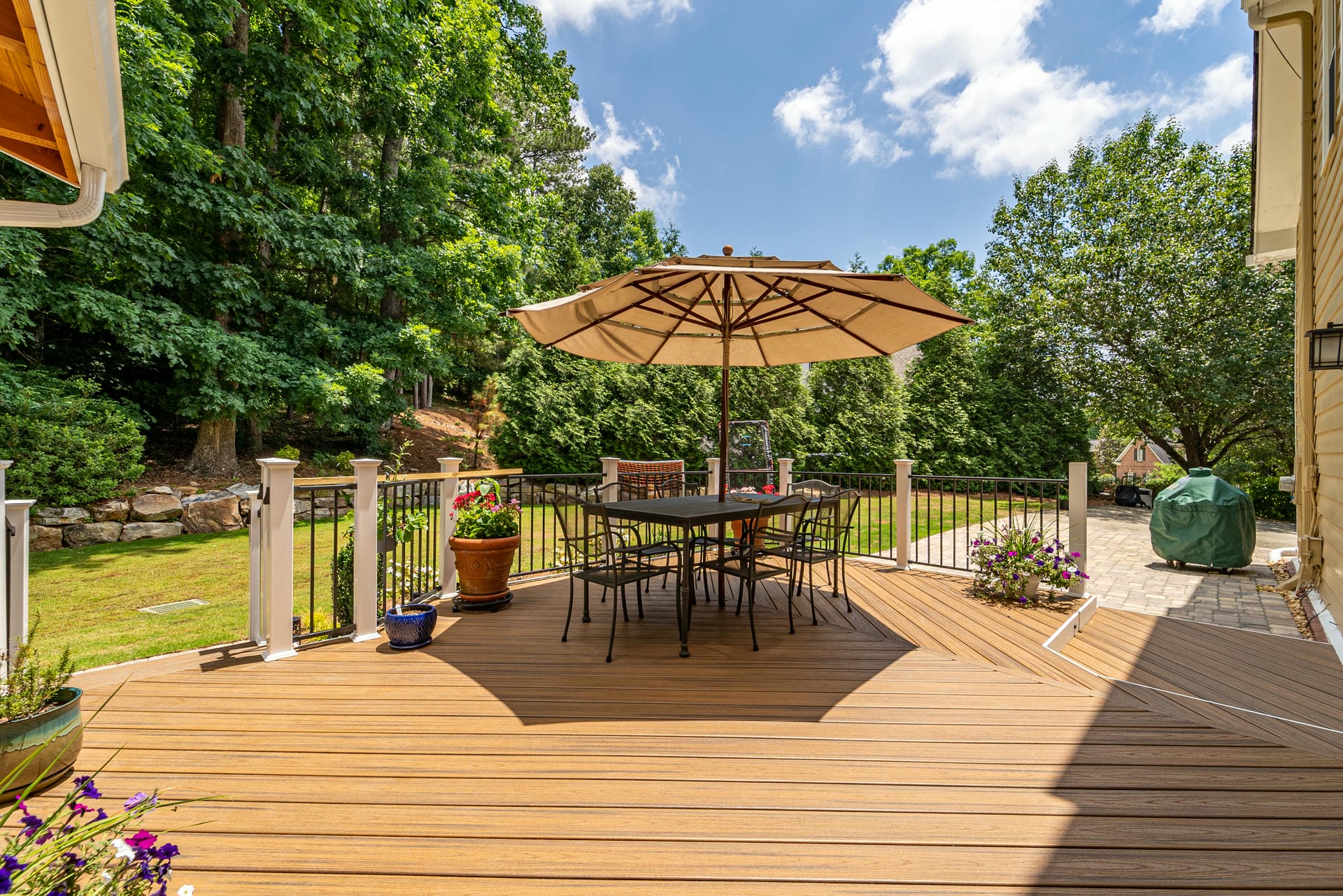Honey toned composite deck with white posts, black metal railing and a shaded dining table