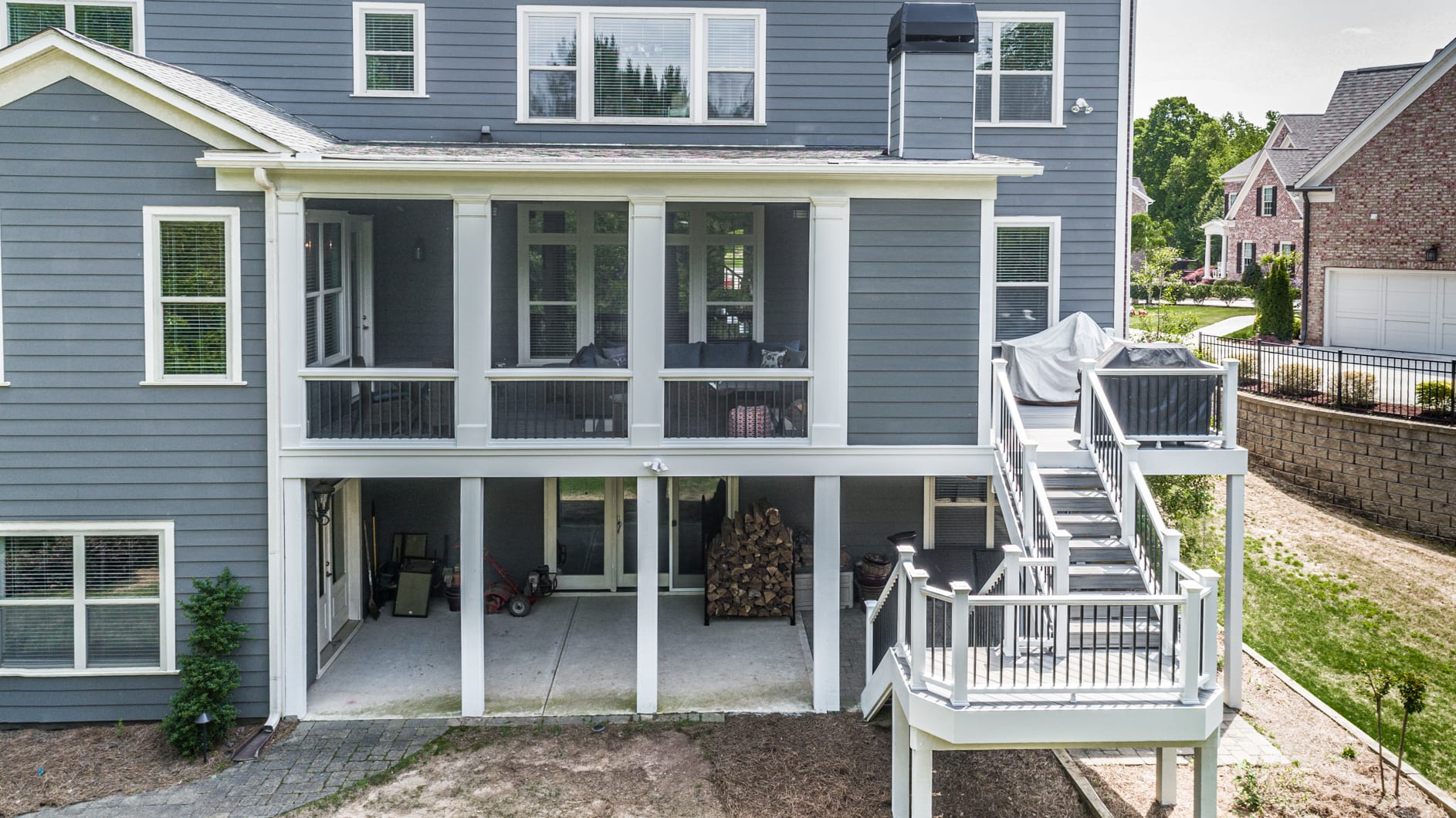 Screened porch with a shed roof on a gray two story home with deck stairs