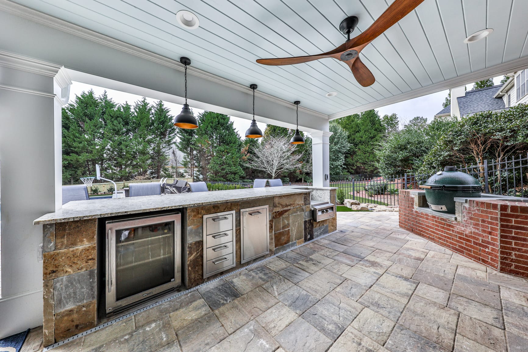 Under deck outdoor kitchen with pendant lighting and a finished white plank ceiling