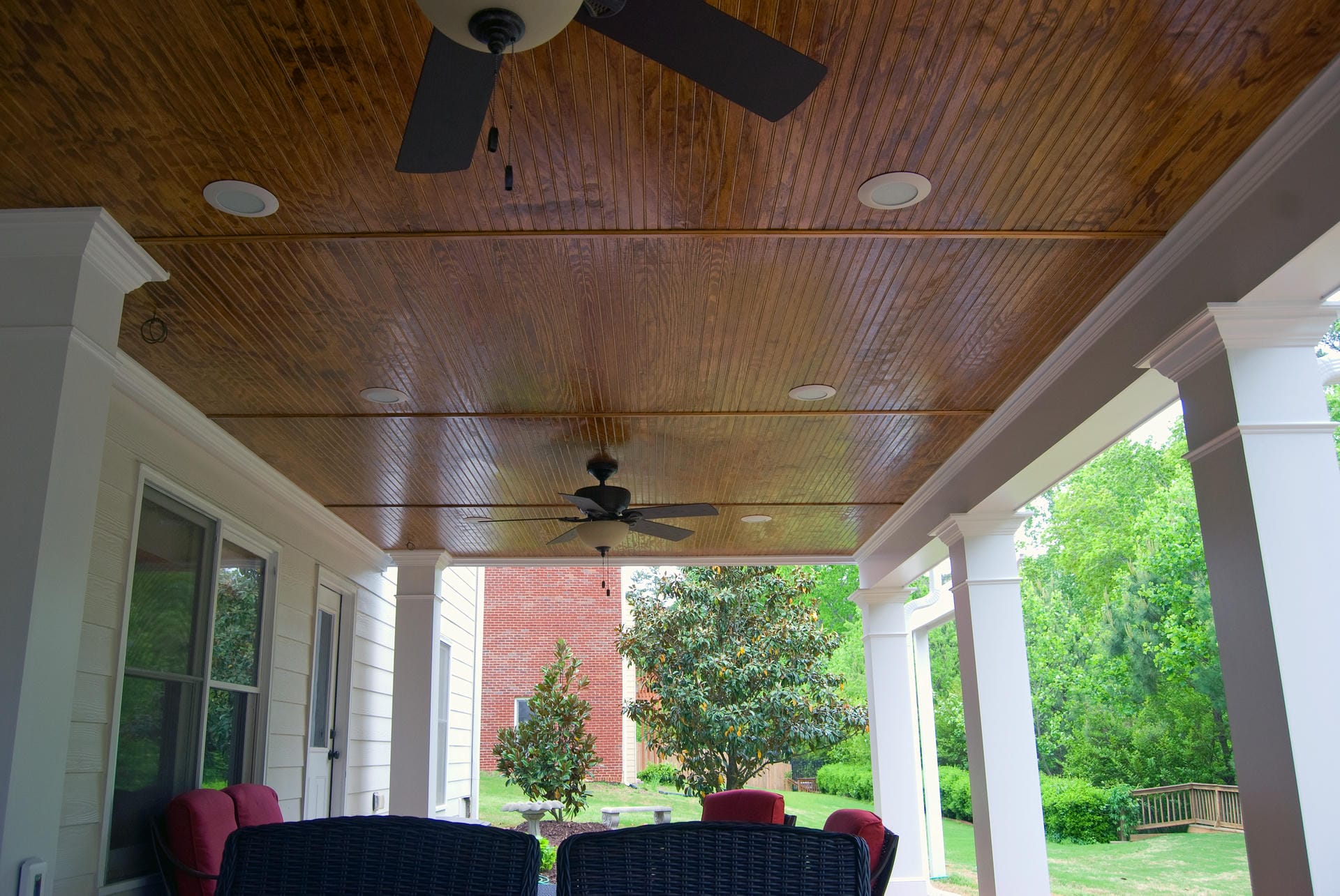 Stained beadboard ceiling under a deck with two ceiling fans and recessed lights