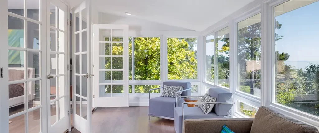 Bright sunroom addition with large windows, French doors, hardwood flooring, and comfortable seating