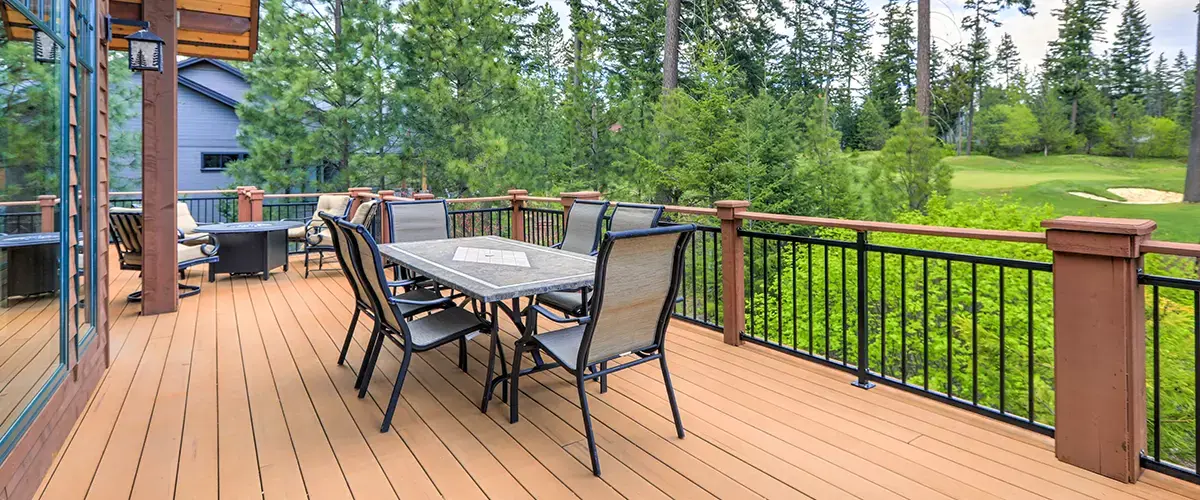 Composite deck with outdoor dining area, black metal railings and scenic wooded backyard