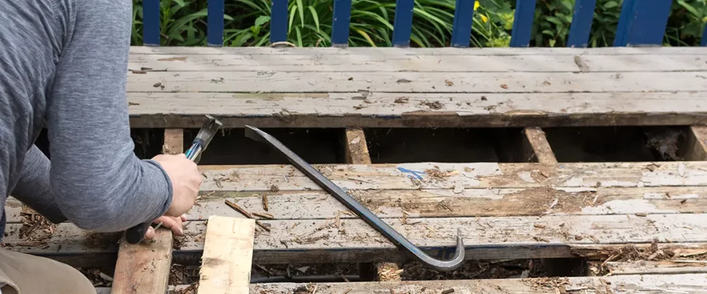 Deck repair contractor removing damaged and rotted wood boards for replacement