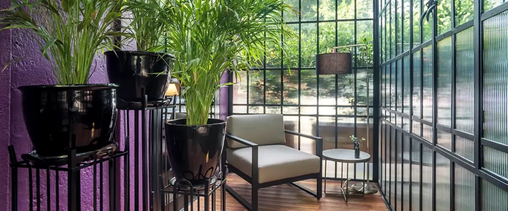 Enclosed sunroom with floor-to-ceiling windows, indoor plants, wood flooring, and lounge seating