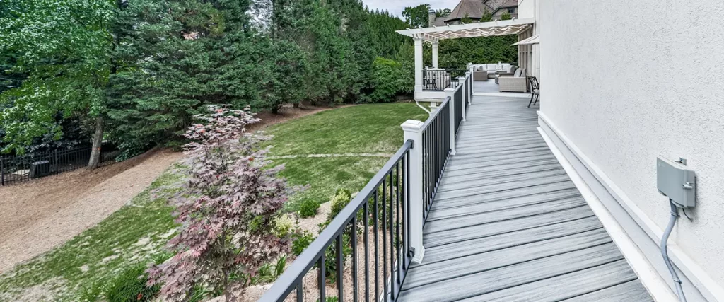 Composite deck with black railing, pergola, and spacious backyard landscaping