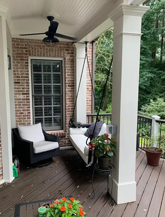 Covered porch with ceiling fan, porch swing, seating and composite decking on a brick home.