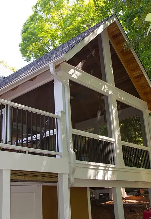 Elevated screened porch and deck addition with gable roof, white columns and black railings.