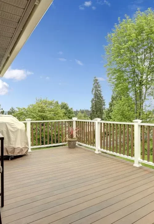 Spacious composite deck with white railings overlooking a green backyard and mature trees